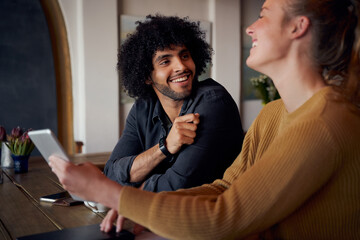 Cheerful man and woman laughing and talking in cafe using digital tablet