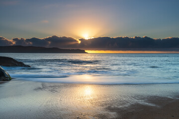 Fototapeta premium Sunrise by the sea with cloud bank and sun rays on the horizon