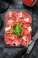 Beef carpaccio on black plate with parmesan cheese and arugula. Black background. Top view