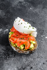 Poached egg on grilled toast with smoked salmon and avocado. Black background. Top view