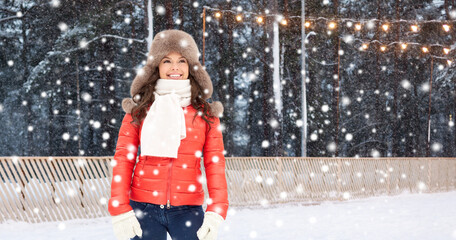 christmas, season and holidays concept - happy woman in winter fur hat over outdoor ice skating rink on background