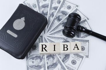 Selective focus of banknotes,holy quran,gavel and cube blocks written with text RIBA.Riba can be...