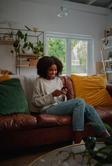 Happy african female relaxing at home browsing and typing on smartphone