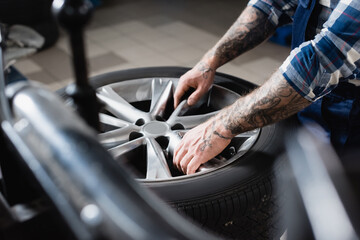 partial view of tattooed repairman taking car wheel in workshop on blurred 
