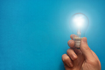 Idea came, flashing concept. Holding burning light bulb in hand against blue background with blank space for text or logo. Copy space. Top view