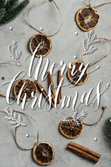 Top view of dried orange pieces with strings, cinnamon sticks and pine branches near merry christmas lettering, stock image