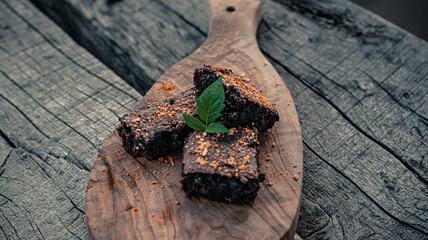 A stack of chocolate brownies on wooden background with mint leaf on top, homemade dessert