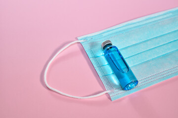 Protective medical mask and glass ampoule with vaccine on a pink background. Face mask and medicine...