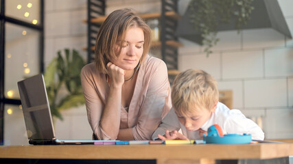 mom helping young son with laptop to do homework. Young woman teaching little boy to use the computer. baby sitter teaching little child girl use laptop application.