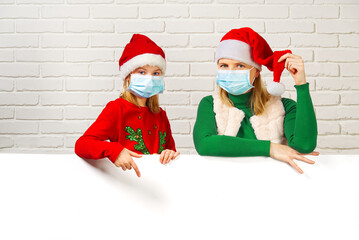 Mother and daughter in medical face mask peeking from behind blank sign billboard assign white brick wall. gnome girl, copy space. covid Christmas concept