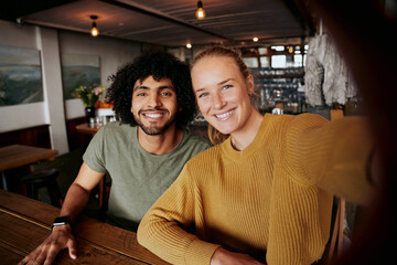 Portrait of smiling young couple relaxing in cafe taking selfie in mobile phone