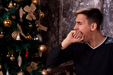 Attractive young guy at the Christmas tree. Gifts.