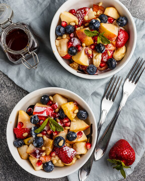 Fruit salad with apples, bananas, strawberries, blueberries, pomegranate seeds, pine nuts, yogurt and honey