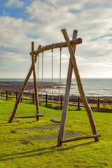 A portrait of a set of swings in a park by the sea at Crail, Fife, Scotland. An empty set of swings in a coastal park in which we encountered while on a staycation. The swings here are empty.