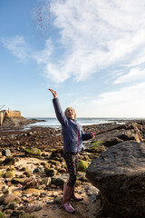 A 10 year old girl with short blond hair is throwing a handful of sand high into the air for fun at the beach in Crail, Fife, Scotland. This was on a short staycation.