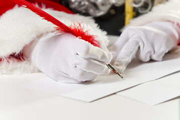 Costumed hands of Santa Claus writing a Christmas letter or greeting on a postcard. close up