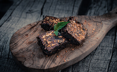 A stack of chocolate brownies on wooden background with mint leaf on top, homemade dessert