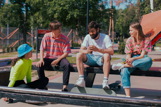 In a good sunny day, group of friends very attractive, multiethnic enjoying the time in a modern, skate park they sitting on the floor and socializing before start to skateboarding