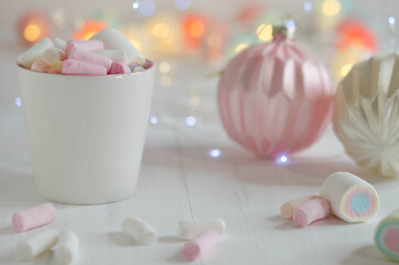 White cup with marshmallows and Christmas balls on a blurred background.