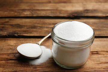 Glass jar and spoon with salt on wooden table, closeup