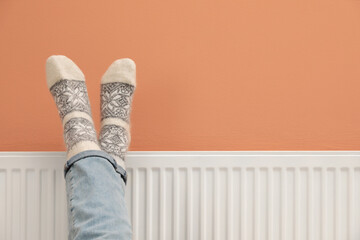 Woman warming legs on heating radiator near color wall, closeup. Space for text