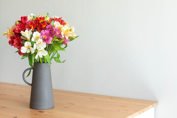 Colorful flowers in a cement vase on a wooden table in grey room with copyspace