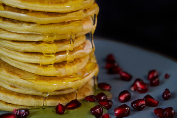 pancakes close-up on a dark background, sprinkled with honey, ready for breakfast, on a turquoise plate with pomegranate berries