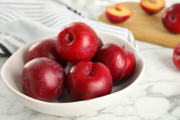 Delicious ripe plums in bowl on white marble table