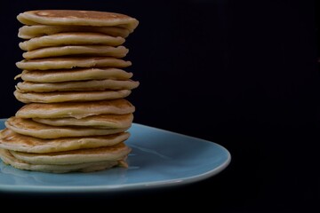 pancakes close-up on a dark background, ready for breakfast, stand in a stack on a turquoise plate