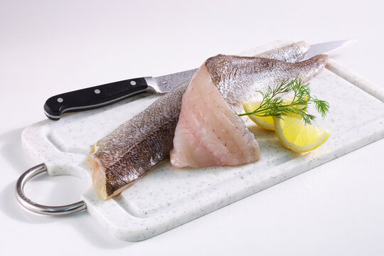 Zander fillets with skin on a board with a knife, lemon and dill