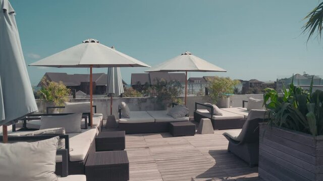 Dollying-in shot of Bali luxurious open terrace with lounging chairs, beach umbrellas, greenery and city view