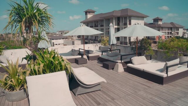 Camera Dolly shot of leisure area on terrace of posh hotel showing chase-lounge, swimming pool and greenery