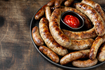Fried sausages. Bavarian and Nuremberg sausages with spices and sauce. Delicious meat sausages in a black ceramic plate on a brown wooden table. German dish	