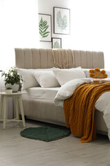 Comfortable bed with knitted orange plaid in stylish room interior