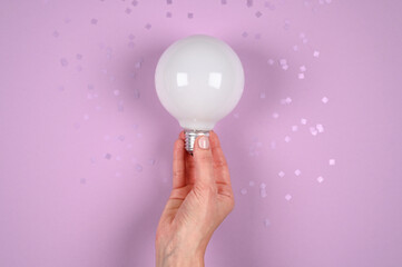 Hand holds a large light bulb on purple background