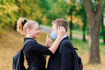 Schoolchildren, a boy and girl in medical masks walk in the city park.