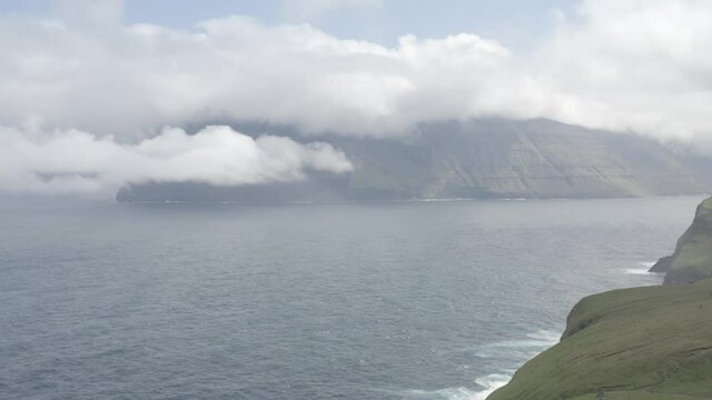 Drone fly over the kallur lighthouse located on Kalsoy Island with green rugged cliff mountain faces on the Faroe Islands in Denmark.