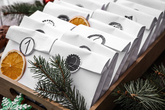 Paper bags in wooden box and festive decor on table, closeup. Christmas advent calendar
