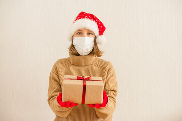 a girl in a santa hat and a medical protective mask holds gifts in her hands. New Year 2021