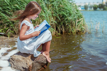 little girl reading a book by the river on a sunny day