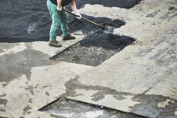 worker repairs asphalt. man throws the asphalt with shovel