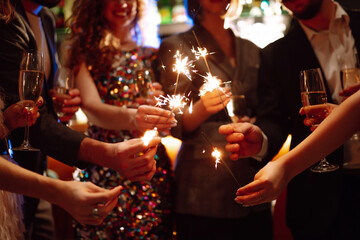 Sparkling sparklers in the hand. Group of happy people holding sparklers at the party. Young friends clinking glasses of champagne in a nightclub. Celebration, people and holidays concept.
