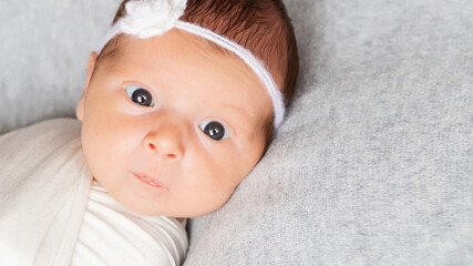 Closeup portrait of cute newborn Caucasian baby. Adorable funny infant child with dark gray eyes and red hair lying on the bed looking at the camera. A genuine candid moment of childhood and lifestyl