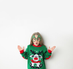 Surprised little girl in Christmas sweater and party glasses on white background