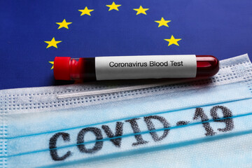 Protective mask and test tube with blood sample on European Union flag background, closeup....