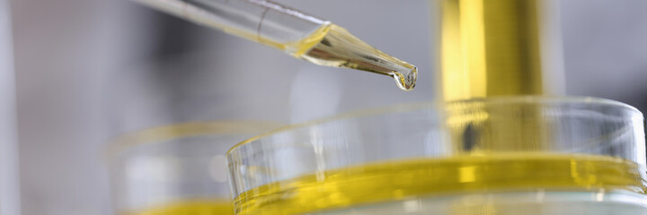 Drop of yellow liquid flows out of glass pipette in chemical laboratory closeup. Quality control of...