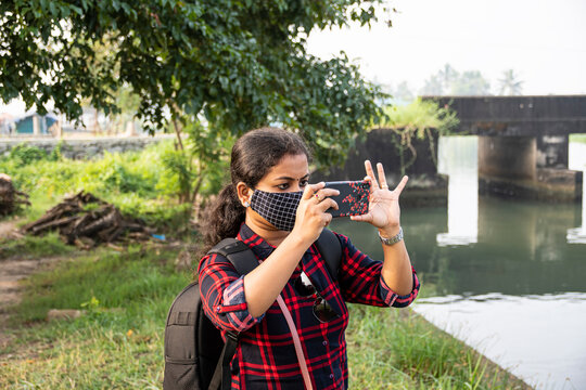 kadamakudy Kerala backpack explorer women wearing face mask taking photos using her phone on white blur green background blurred