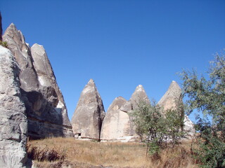 Panorama of sharp-topped triangular rocks against a clear blue sky surrounded by poor desert vegetation.