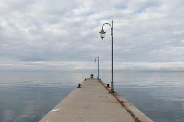 man on wheelchair fishing at the end of the pier far away on horizon rod line cloudy in greece