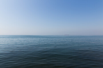 seascape of aegean sea with a faint hazy tanker ship boat in the horizon. blue sky no clouds with blue sea with some small ripple waves